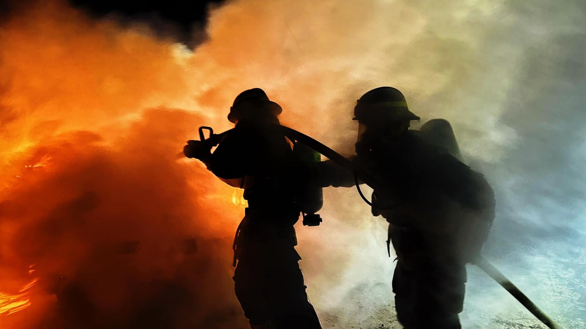 Two firefighters with extinguisher in front of fire