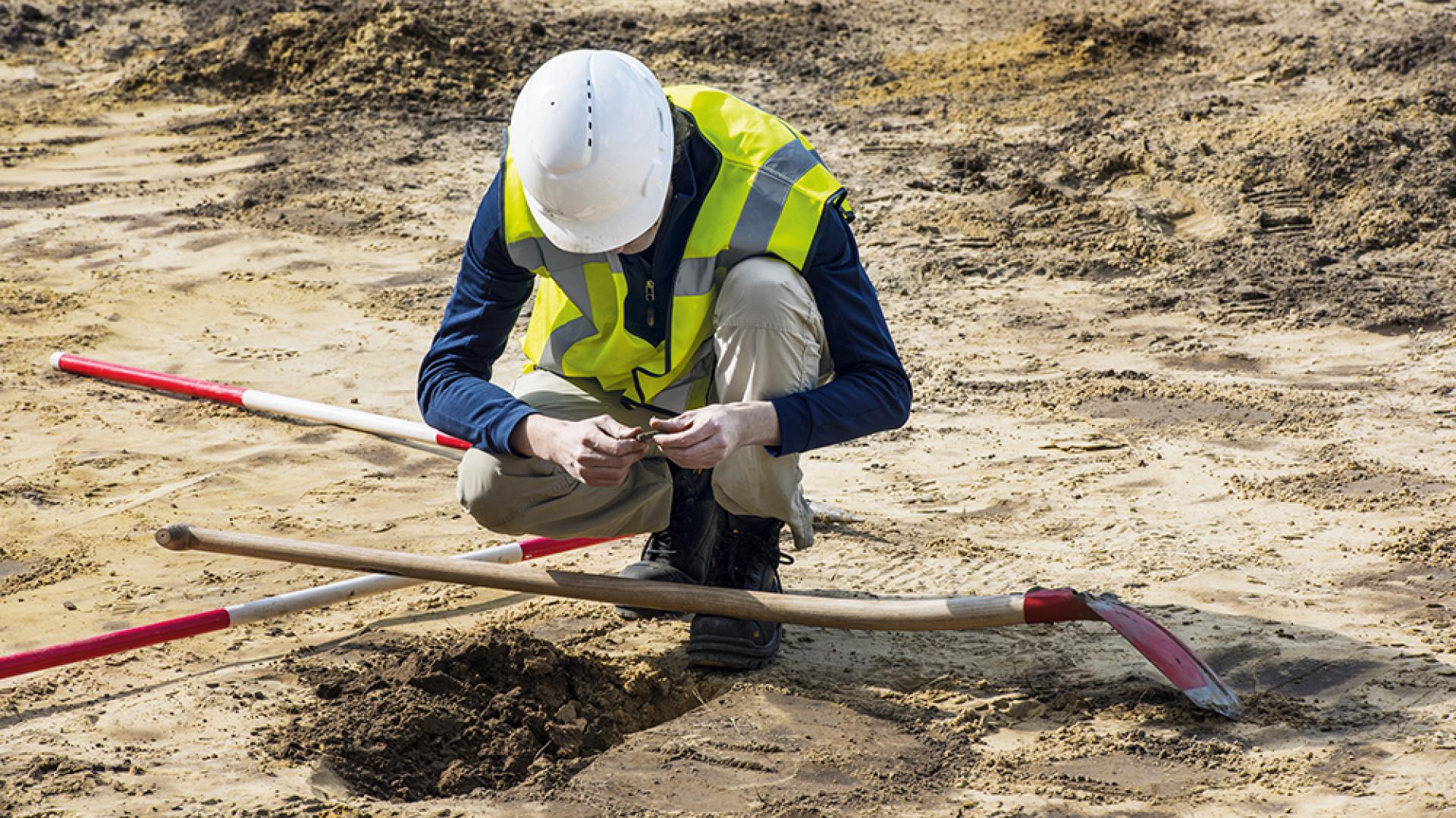 Archaeologist with equipment crouched on ground