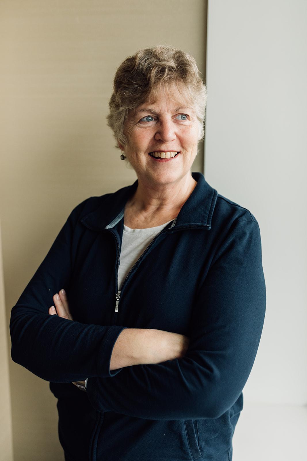Elderly woman with short hair smiling and crossing her arms.