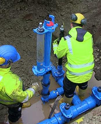 Two workers in bright safety gear repairing a water main.